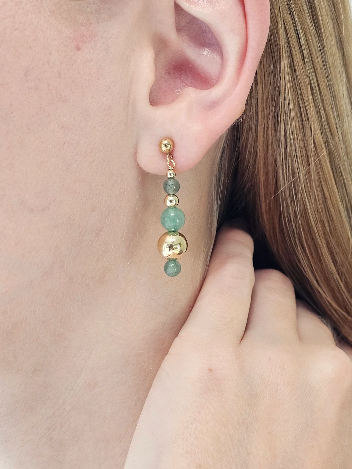 Gold and green beaded earring on ear.
